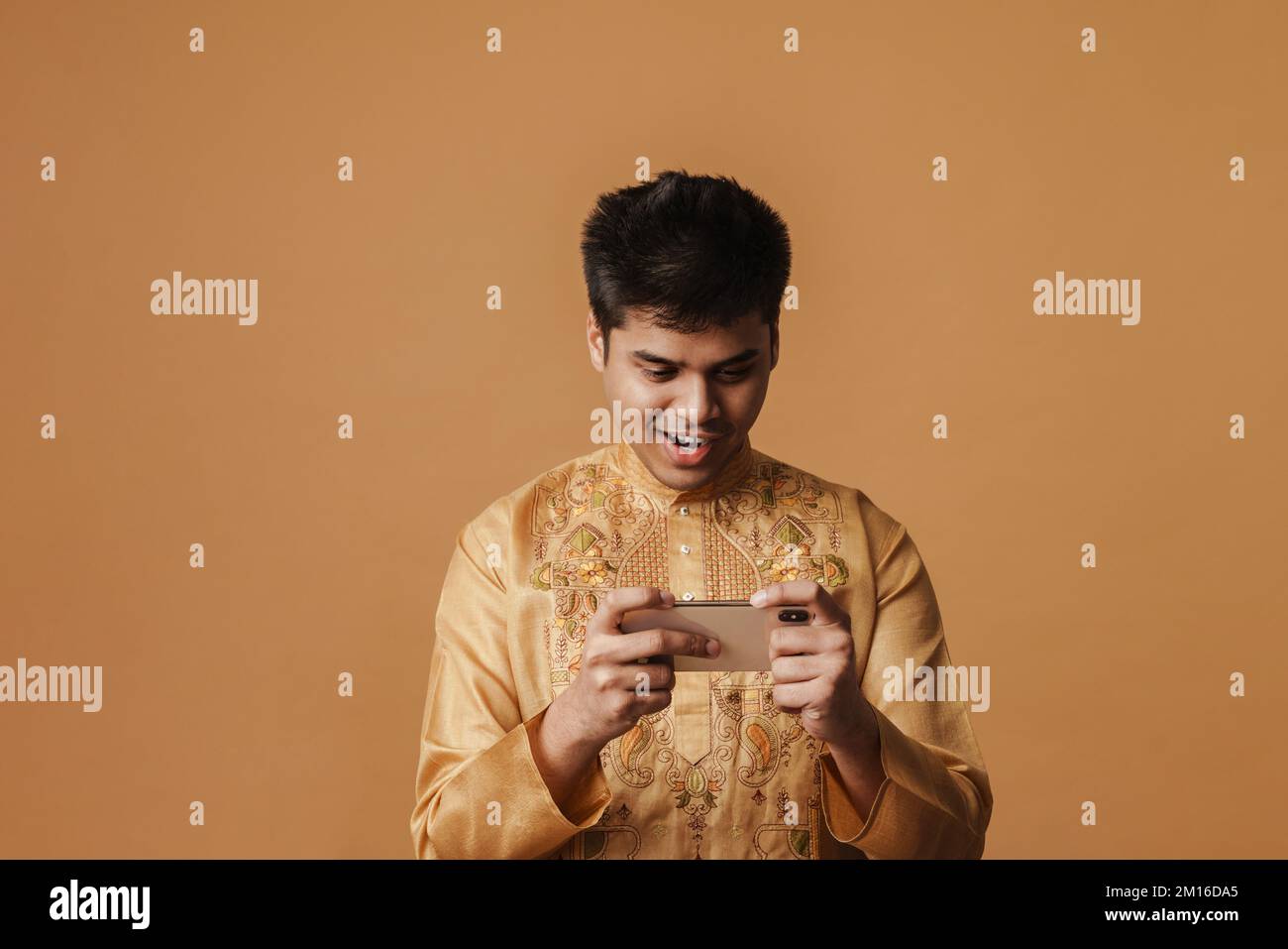 Junger brauner indianer, der lächelt und ein Handy benutzt, isoliert auf gelbem Hintergrund Stockfoto