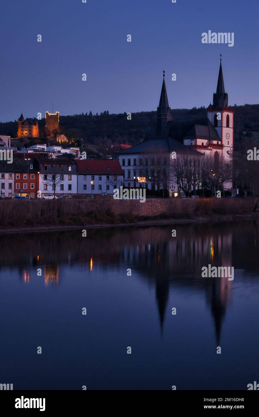 Bingen am Rhein, Deutschland - 10. Januar 2021: Kirche und Reflexion am Rhein mit Schloss Klopp auf einem Hügel im Hintergrund beleuchtet bei Nacht Stockfoto