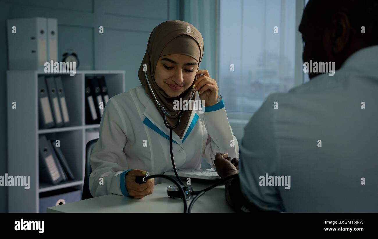 Arabian Frau Ärztin Krankenschwester misst hohen niedrigen Blutdruck verwenden Tonometer Listen Puls von afrikanischen Patienten leiden Bluthochdruck Herzkrankheit weiblich Stockfoto