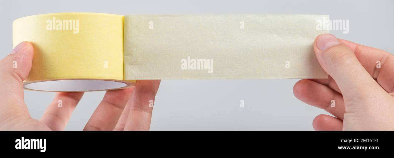 Papierklebeband auf weiß isoliert. Eine Rolle Papierklebeband in den Händen eines weißen Mannes. Ungefaltetes Klebeband mit Platz für Text. Stockfoto