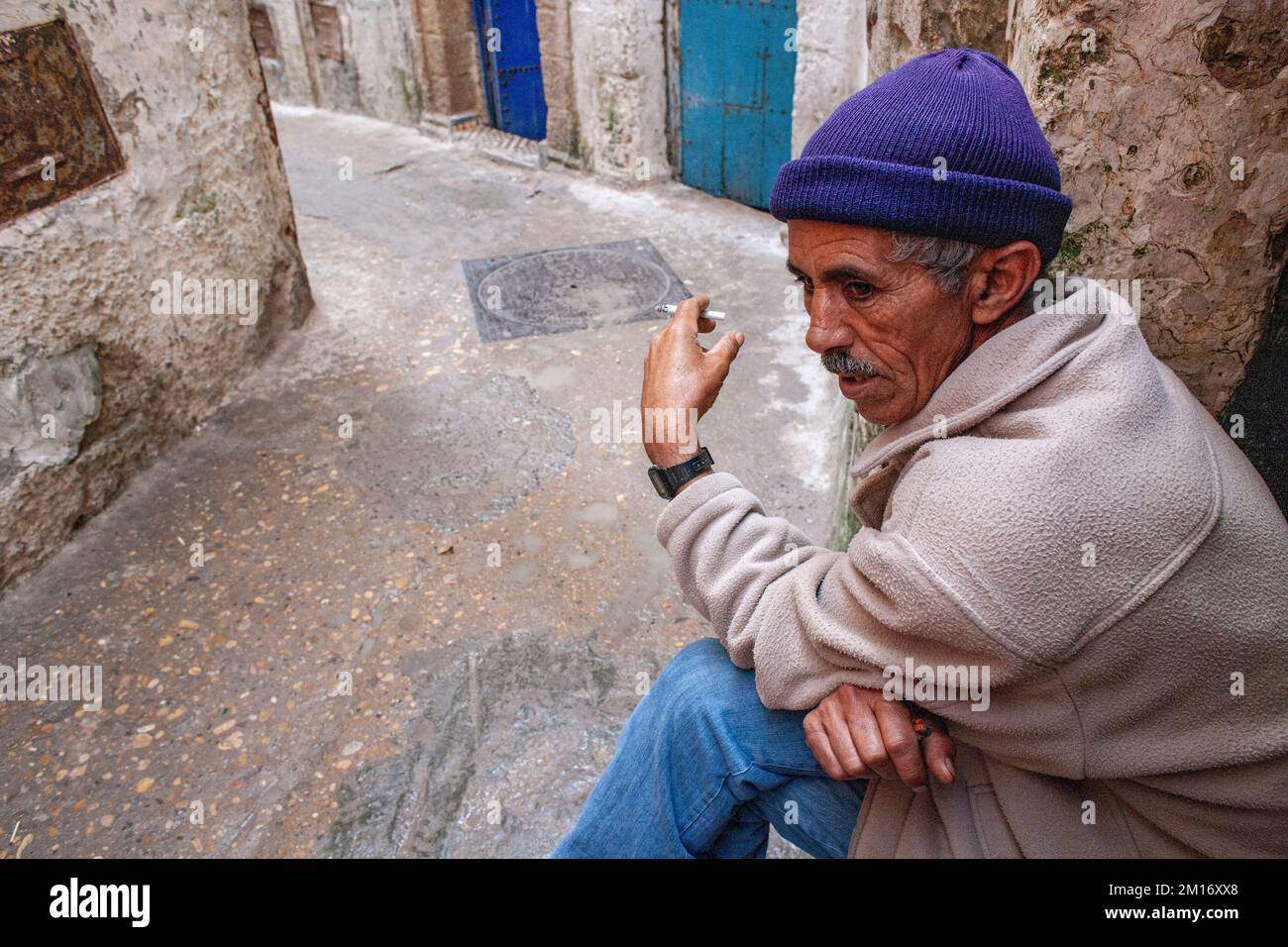Ein Mann sitzt in einer engen Straße und farbenfrohen alten Häusern der mittelalterlichen Medina von Essaouira, Stockfoto
