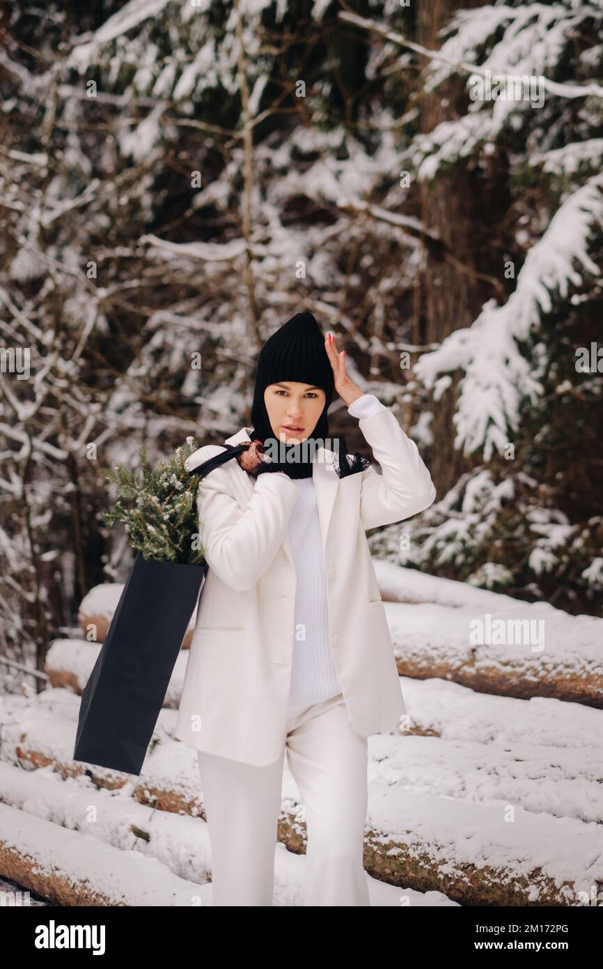 Ein Mädchen in einem weißen Anzug und Balaklava mit einem Paket Weihnachtsbäume im Winterwald an Silvester. Neujahrskonzept Stockfoto
