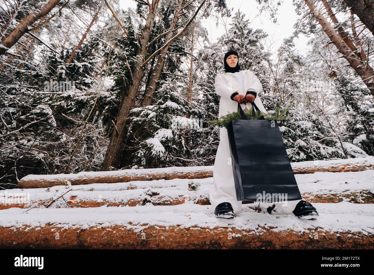 Ein Mädchen in einem weißen Anzug und Balaklava mit einem Paket Weihnachtsbäume im Winterwald an Silvester. Neujahrskonzept Stockfoto