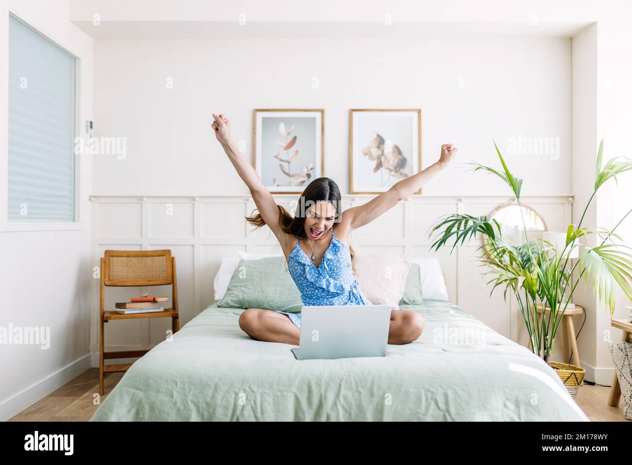 Aufgeregte junge Erwachsene Frau, die mit einem Notebook im Bett sitzt und ihren Erfolg feiert Stockfoto