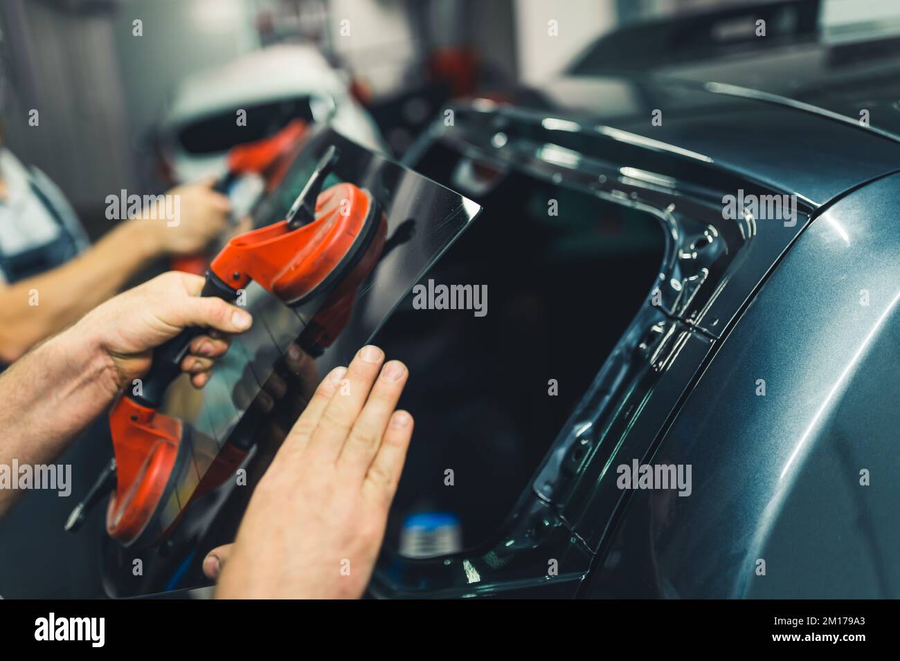 Ausbau der Windschutzscheibe oder Heckscheibe unter Verwendung von Saugnäpfen. Nahaufnahme im Innenbereich. Zwei kaukasische, nicht erkennbare Mechaniker reparieren ein Fahrzeug. Hochwertiges Foto Stockfoto
