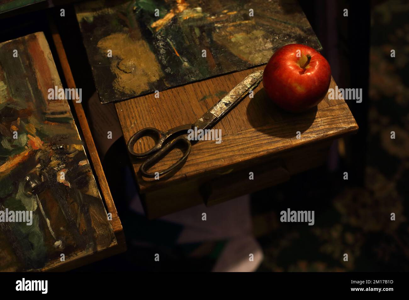 Stilleben mit klassischer schwarzer Schere und Apfel mit Gemälden im Kunststudio Stockfoto