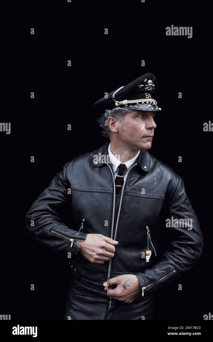 Rocker in Café Racer-Ausrüstung mit schwarzer Lederjacke und Servicehut Stockfoto