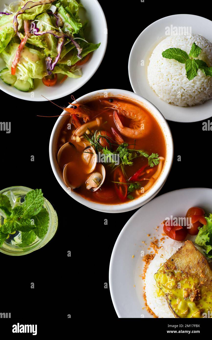 Mittagsset aus tom Yum Suppe, Salat, gegrilltem Basa-Fisch, Reis, Limonade auf schwarzem Hintergrund Stockfoto