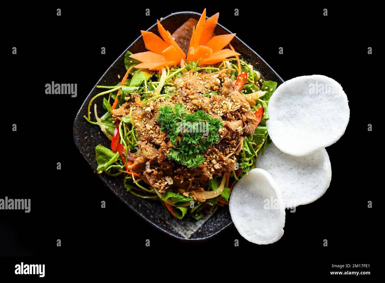 Asiatischer Rindersalat mit Indianerblättern serviert mit Reischips auf schwarzem Hintergrund Stockfoto