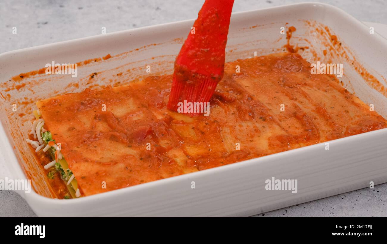Lasagne zusammenbauen. Die letzte Lasagne mit Marinara-Sauce überziehen. Rezept für Spinat-Lasagne Stockfoto