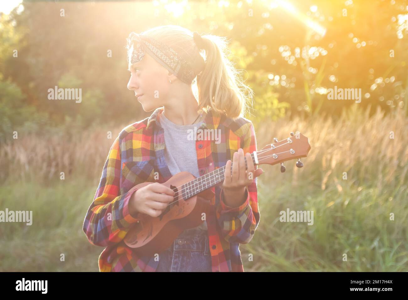 Unschärfe-Mädchen mit Gitarre bei Sonnenuntergang. Ein Mädchen, das in der Natur herumläuft. Ein kleines Mädchen draußen auf der grünen Wiese. Sommerzeit. Ein Volkskünstler Stockfoto
