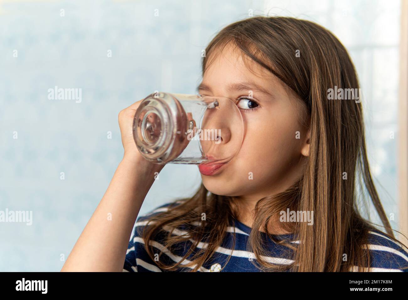 Ein kleines Mädchen trinkt Wasser aus einem Glas Tasse. Kleines Mädchen hält ein Glas Wasser. Durst nach Wasser Stockfoto