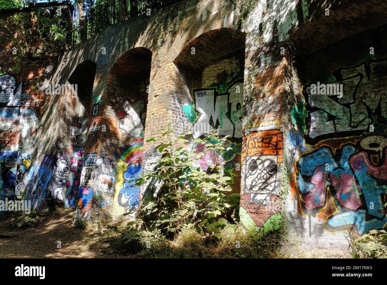 Farbenfrohe bemalte Graffiti auf alten, stillgelegten Backsteinbögen in der Sonne entlang des Parkland Walk in der Nähe von Finsbury, Archway und Highgate, London, England Stockfoto