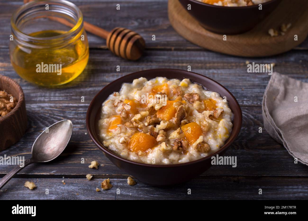 Köstlicher Haferbrei mit gebackenem Kürbis, Honig und Nüssen in einer Keramikschüssel auf einem Holztisch. Gesundes, hausgemachtes Frühstück. Selektiver Fokus Stockfoto