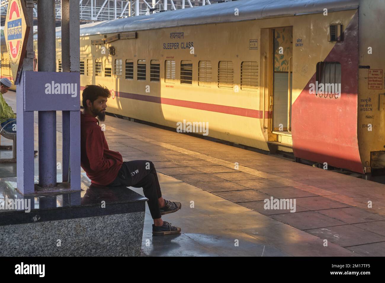 Ein junger Indianer, ein Eisenbahnpassagier, sitzt vor einem Fernzug am Chhatrapati Shivaji Maharaj Terminus in Mumbai, Indien Stockfoto