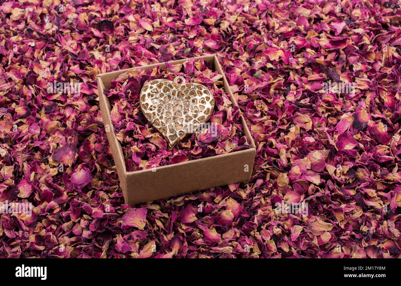 Goldenes Herz auf einer Schachtel voller Blütenblätter Stockfoto