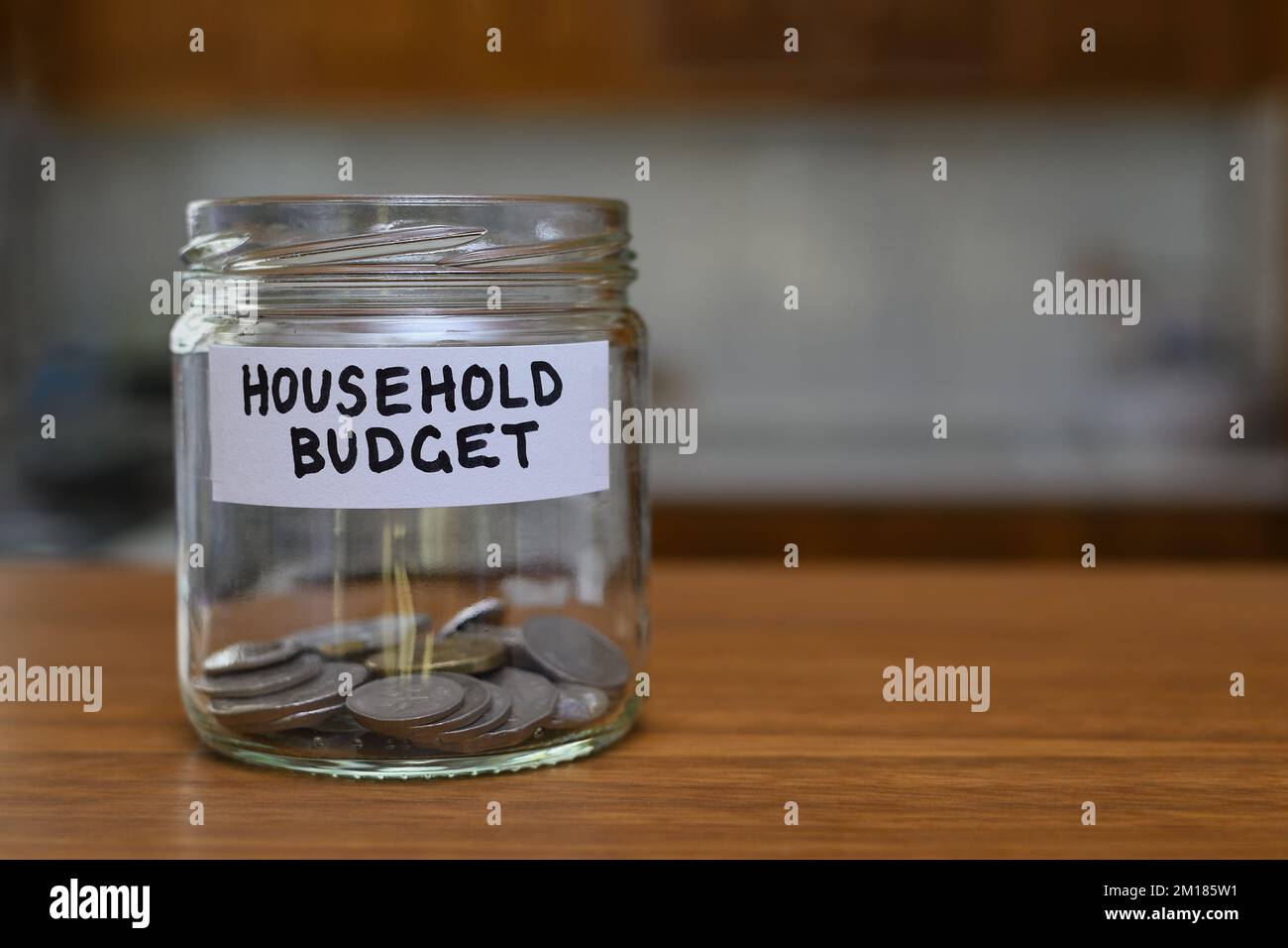 Ein Haushaltsbudgetzeichen auf einem Glasglas mit nur einer Handvoll Münzen, das den Geldmangel veranschaulicht, von dem manche leben müssen Stockfoto