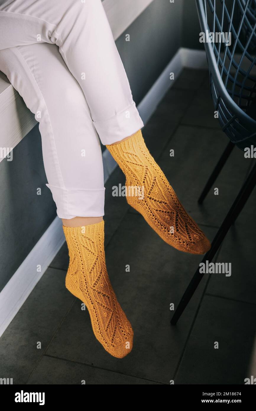 Weibliche Beine in weißen Hosen und gelben Stricksocken. Gemütliche Zeit Stockfoto