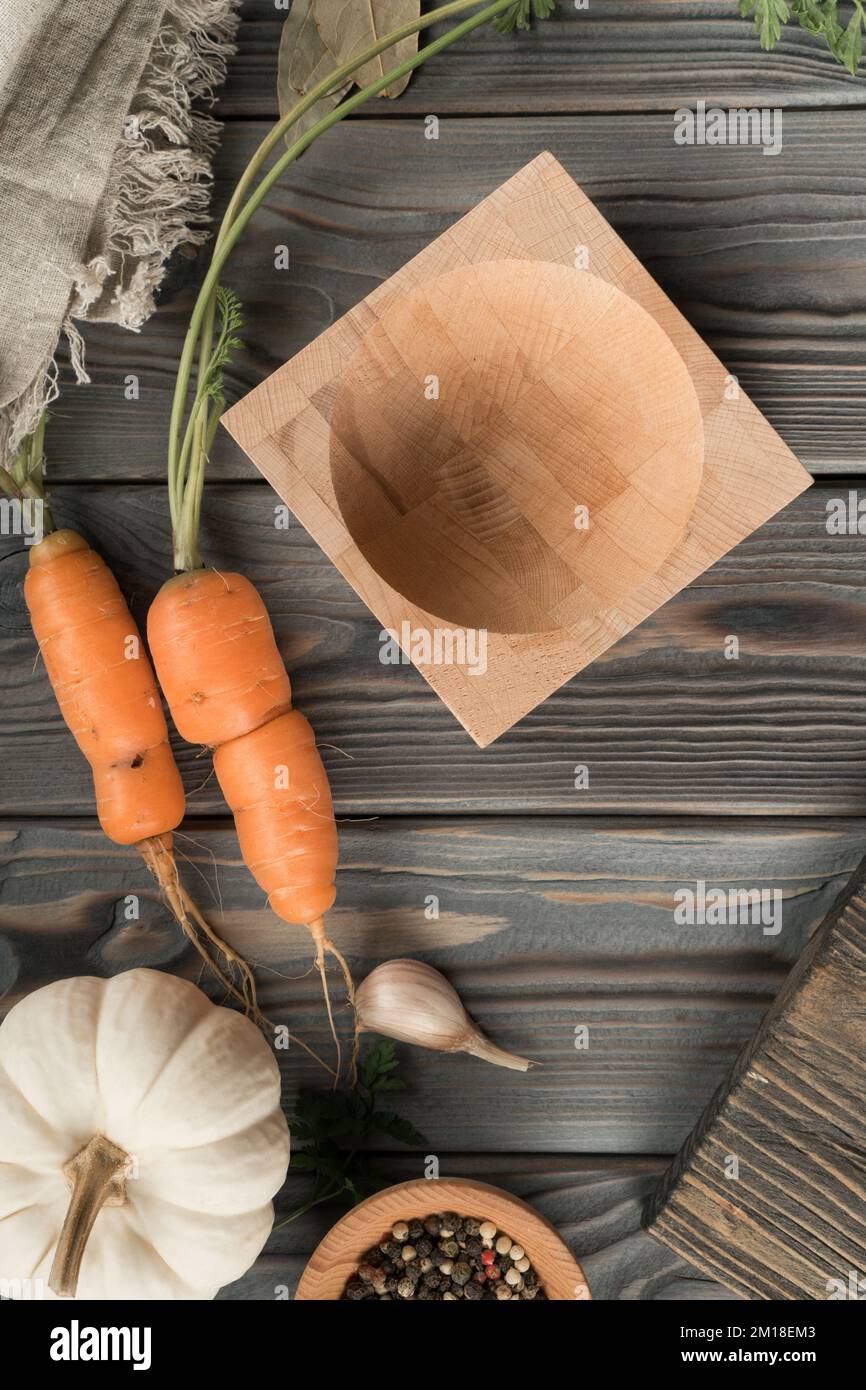 Reife ungeschälte Orangenkarotte mit grünem Transport. Leere Schüssel auf dem Küchentisch aus Holz. Flache Lay-Ansicht. Anordnung von frischem Gemüse und Aromen. Fertig machen Stockfoto