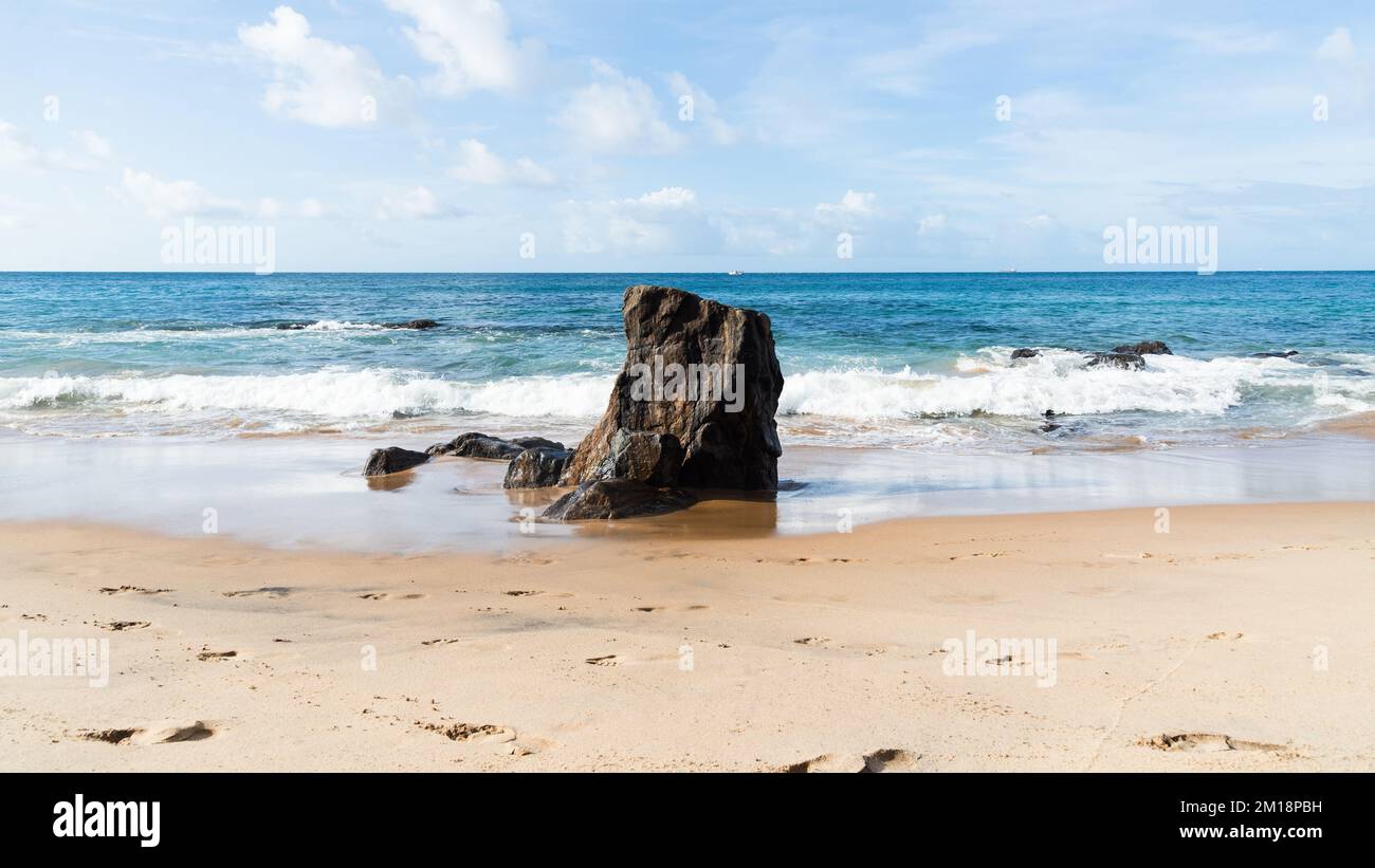 Während eines Vorhangs am Meer bricht eine Welle um einen Felsen. Farol da Barra Beach, Salvador, Brasilien. Stockfoto