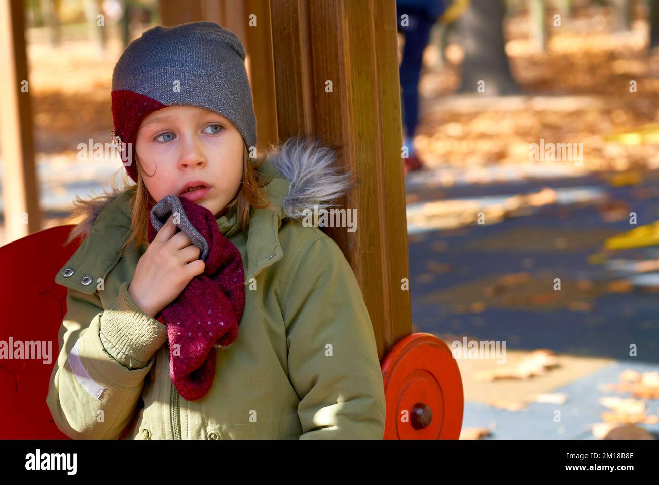 Beleidigtes, verängstigtes Kind in einer Jacke und einem Hut auf einem Herbstspielplatz Stockfoto