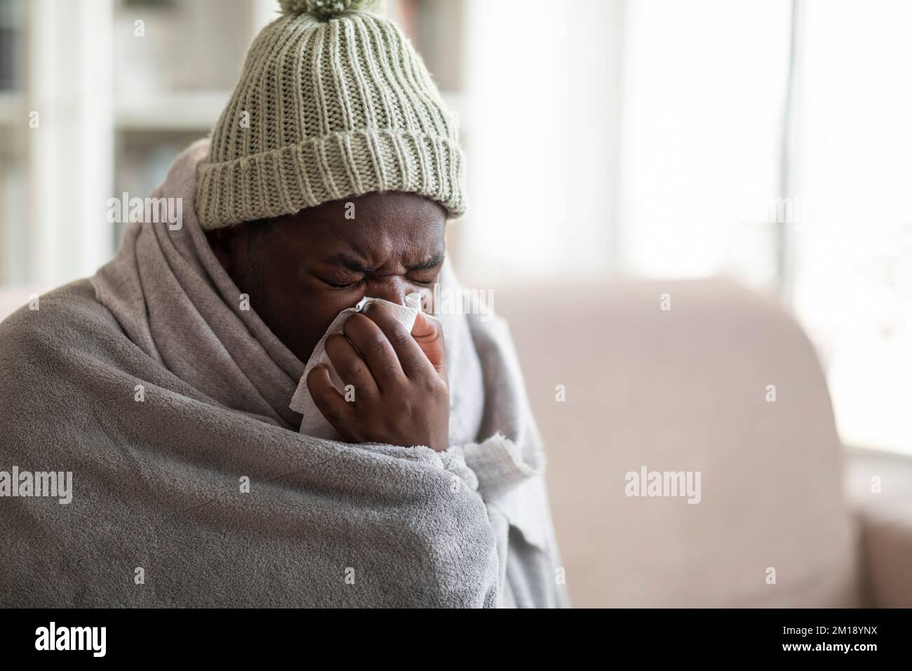 Eine Nahaufnahme eines kranken Schwarzen, der mit einer Decke bedeckt ist, die niest Stockfoto