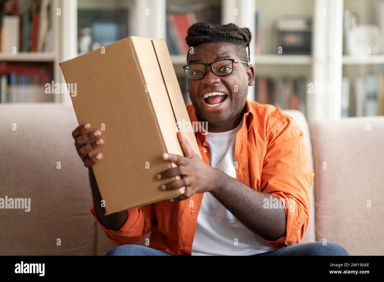 Aufgeregter fetter afrikanischer Kunde erhält gutes Paket, Heim-Innenraum Stockfoto