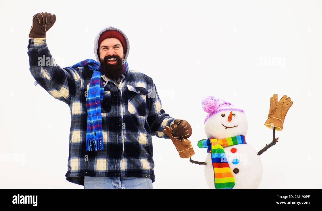Ein bärtiger Mann in Winterkleidung hält den Schneemann mit der Hand. Wintermode. Schneemann mit Hut, Schal, Handschuhen. Stockfoto