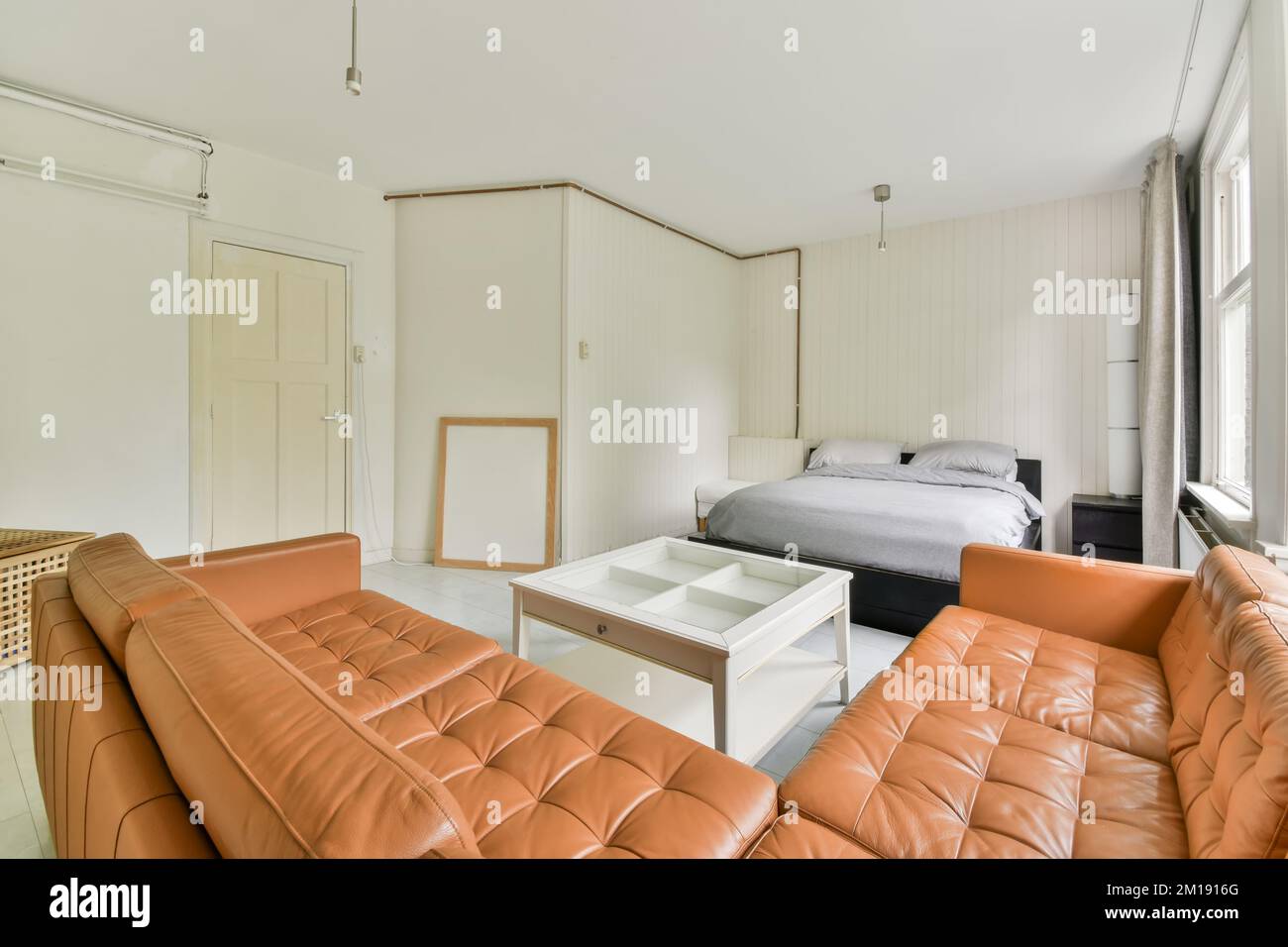 Ein Wohnzimmer mit orangefarbenen Ledersofas und einem weißen Couchtisch in der Mitte des Zimmers ist ein Bett Stockfoto