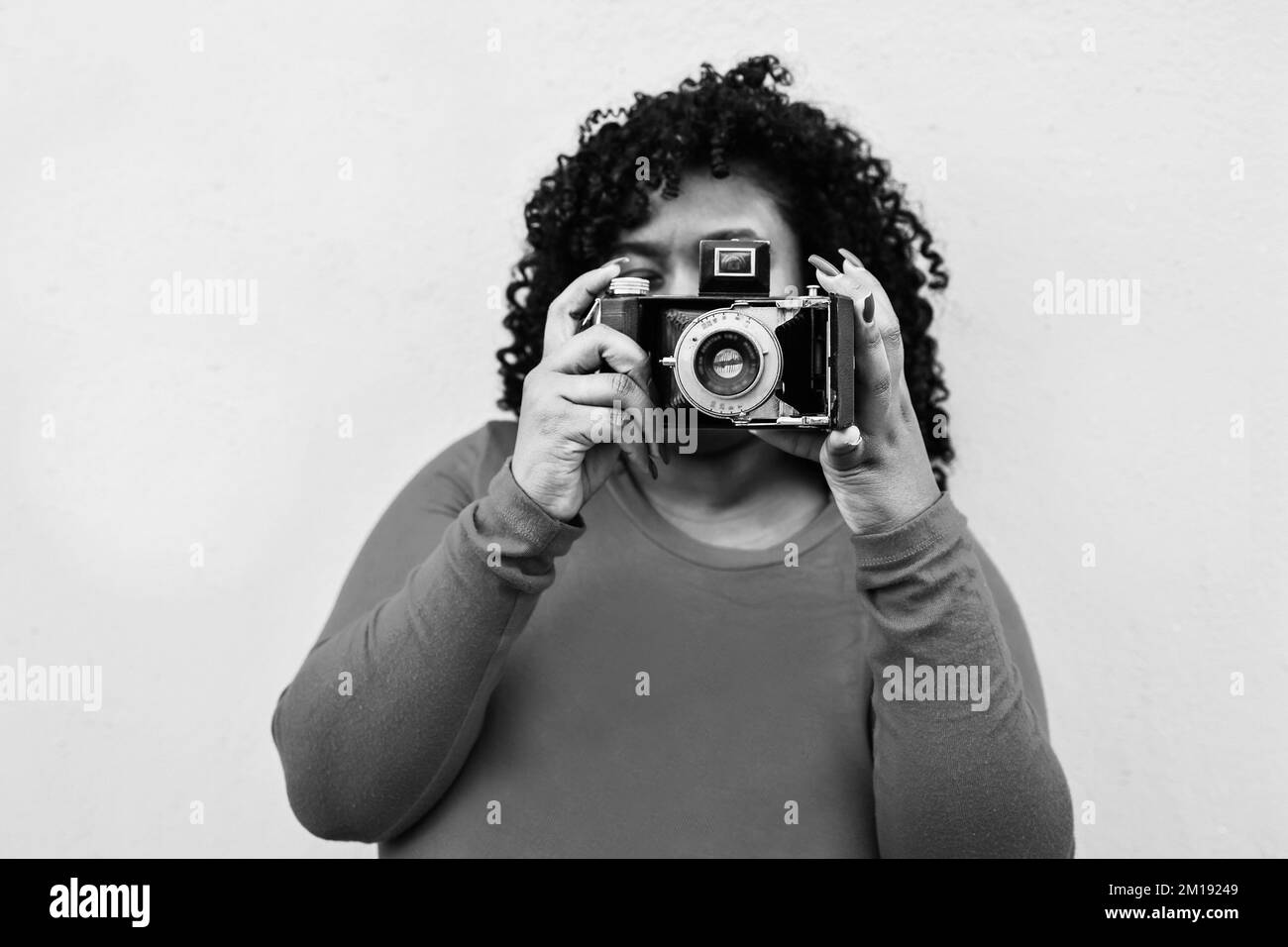Kurvige afrikanische Frau, die im Freien eine Oldtimer-Kamera verwendet – Fokus auf das Fotoobjektiv – Schwarz-Weiß-Bearbeitung Stockfoto