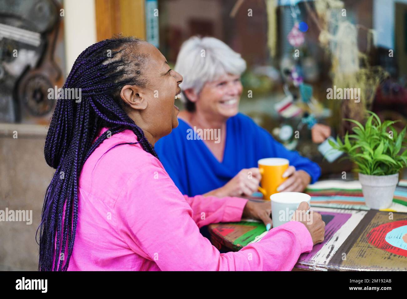 Ältere Freunde aus verschiedenen Rassen treffen sich und unterhalten sich an der Bar im Freien, während sie gemeinsam Kaffee trinken - konzentrieren Sie sich auf das gesicht afrikanischer Frauen Stockfoto