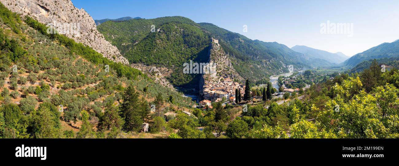 Panoramablick im Sommer auf das Dorf Entreveaux in der Provence mit Olivenbaumfeldern und dem Fluss Var. Alpes-de-Haute-Provence, Alpen, Frankreich Stockfoto
