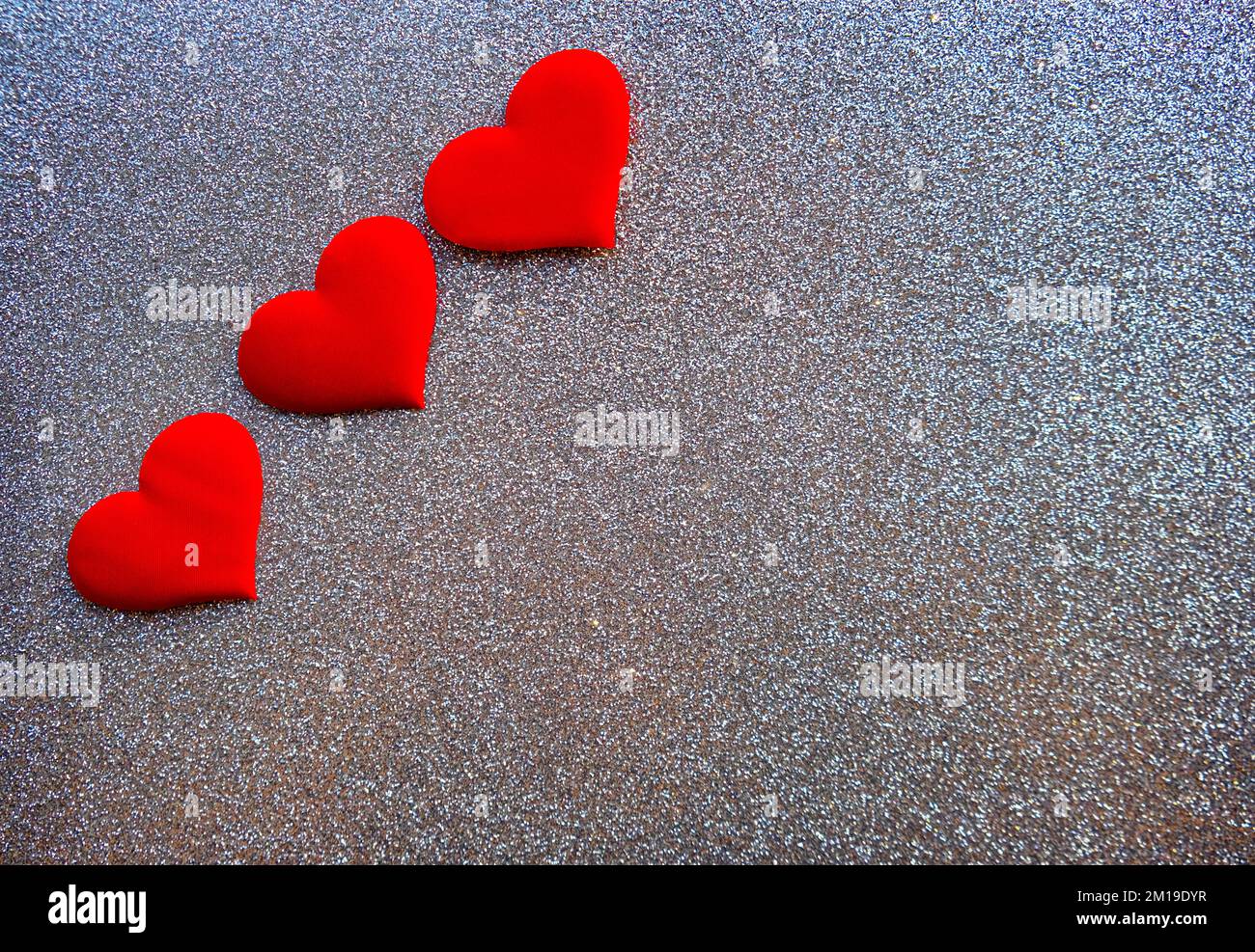 Drei rote dekorative Herzen auf glitzerndem silbernen Hintergrund mit Kopierbereich. Valentinskarte. Stockfoto