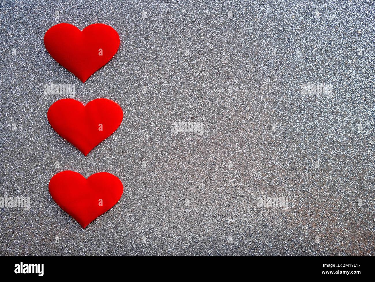 Drei rote dekorative Herzen auf glitzerndem silbernen Hintergrund mit Kopierbereich. Valentinskarte. Stockfoto