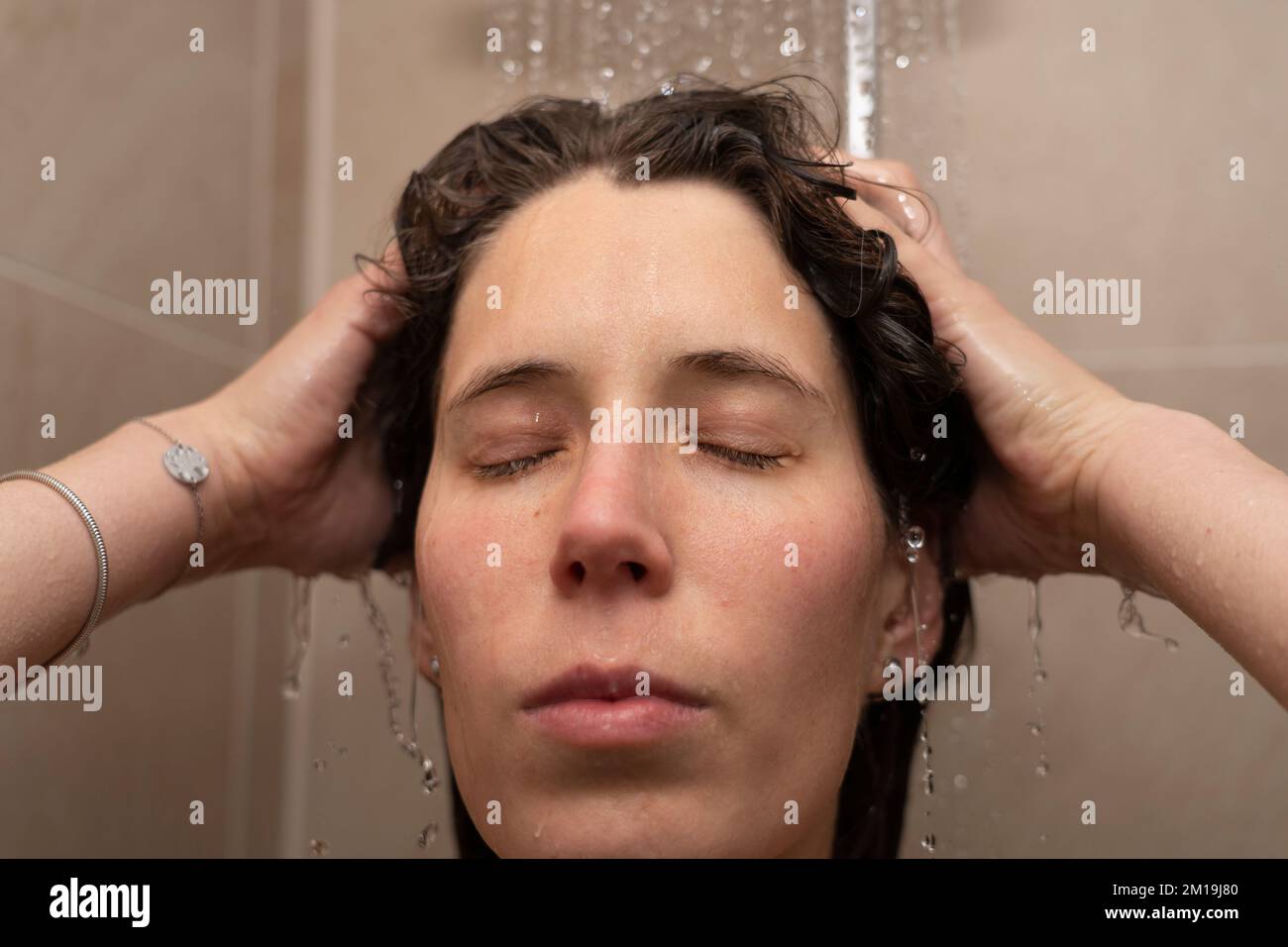 Eine Frau in ihren Dreißigern wäscht sich die Haare in der Dusche mit geschlossenen Augen. Konzept: An das Leben denken, entspannen Stockfoto