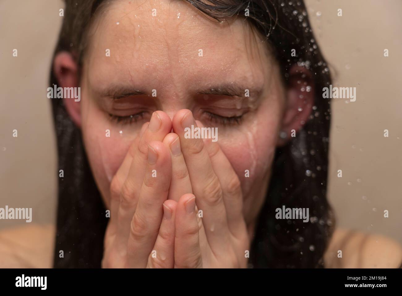 Eine junge Frau unter der Dusche, mit Wasser, das ihr emotionales Gesicht runterläuft. Konzept: Bipolare Störung, psychische Gesundheit, Traurigkeit, Niedergeschlagenheit, Traurigkeit Stockfoto