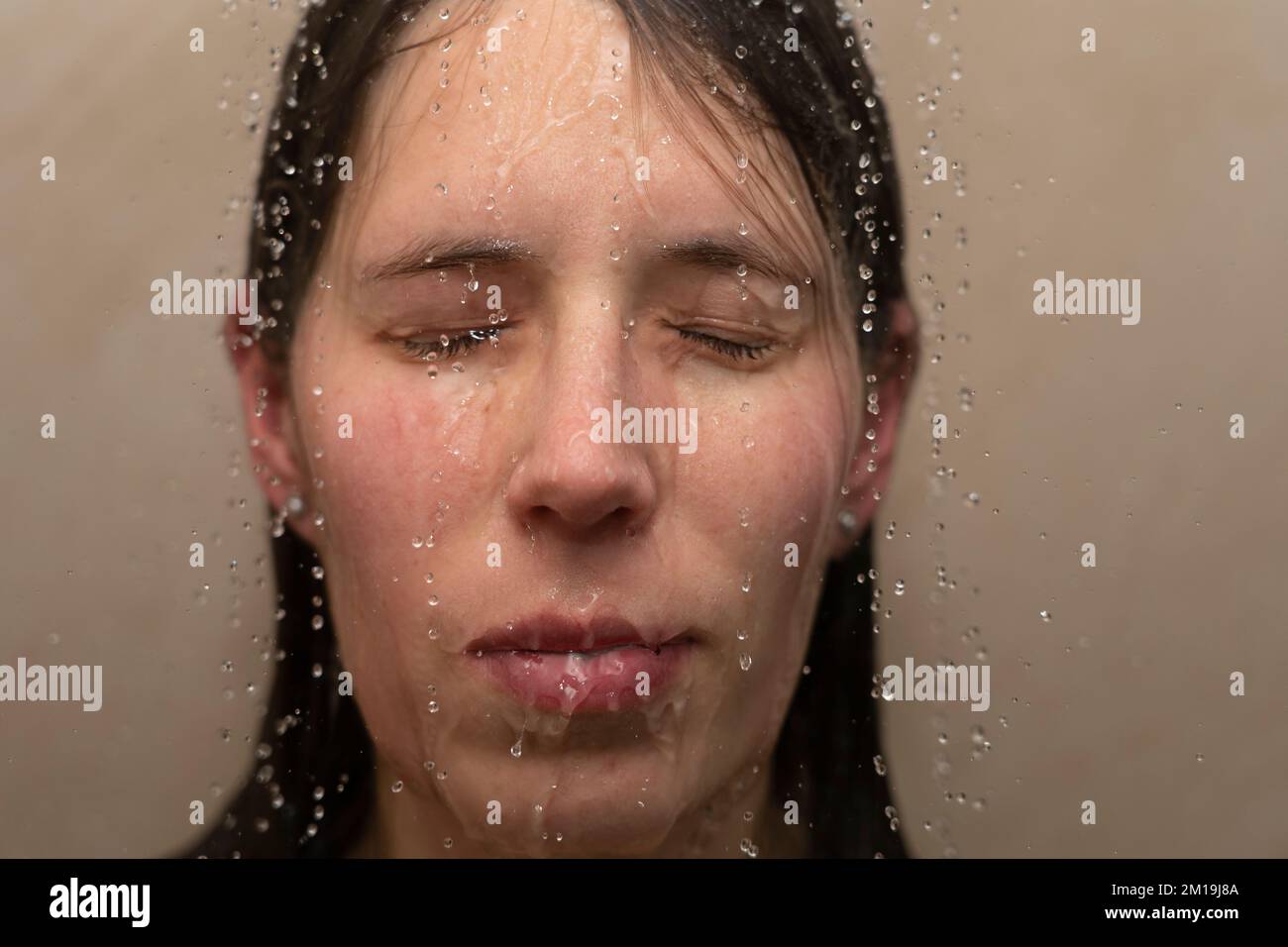 Eine junge Frau unter der Dusche, mit Wasser, das ihr ins Gesicht läuft. Konzept: Psychische Gesundheit, Ängste, Ängste, Gefühl gebrochen, körperdysmorphe Störung Stockfoto