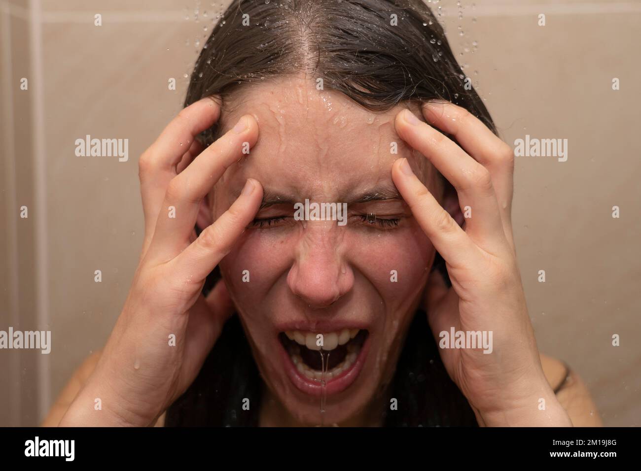 Eine junge Frau unter der Dusche, mit Wasser, das ihr emotionales Gesicht runterläuft. Konzept: Wütend, kann es nicht mehr ertragen, psychische Probleme, moderner Lebensstress Stockfoto