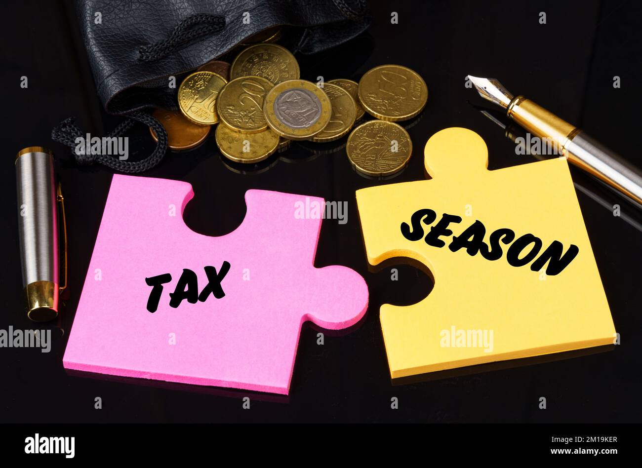 Geschäfts- und Finanzkonzept. Münzen sind auf der schwarzen Oberfläche verstreut, es gibt einen Stift und Rätsel, auf denen sie geschrieben sind - STEUERSAISON Stockfoto