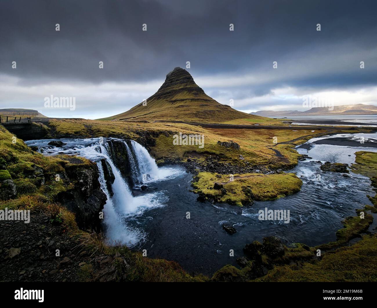 Wasserfall mit bewölktem Himmel und grünem Gras in Island. Kirkjufell Stockfoto