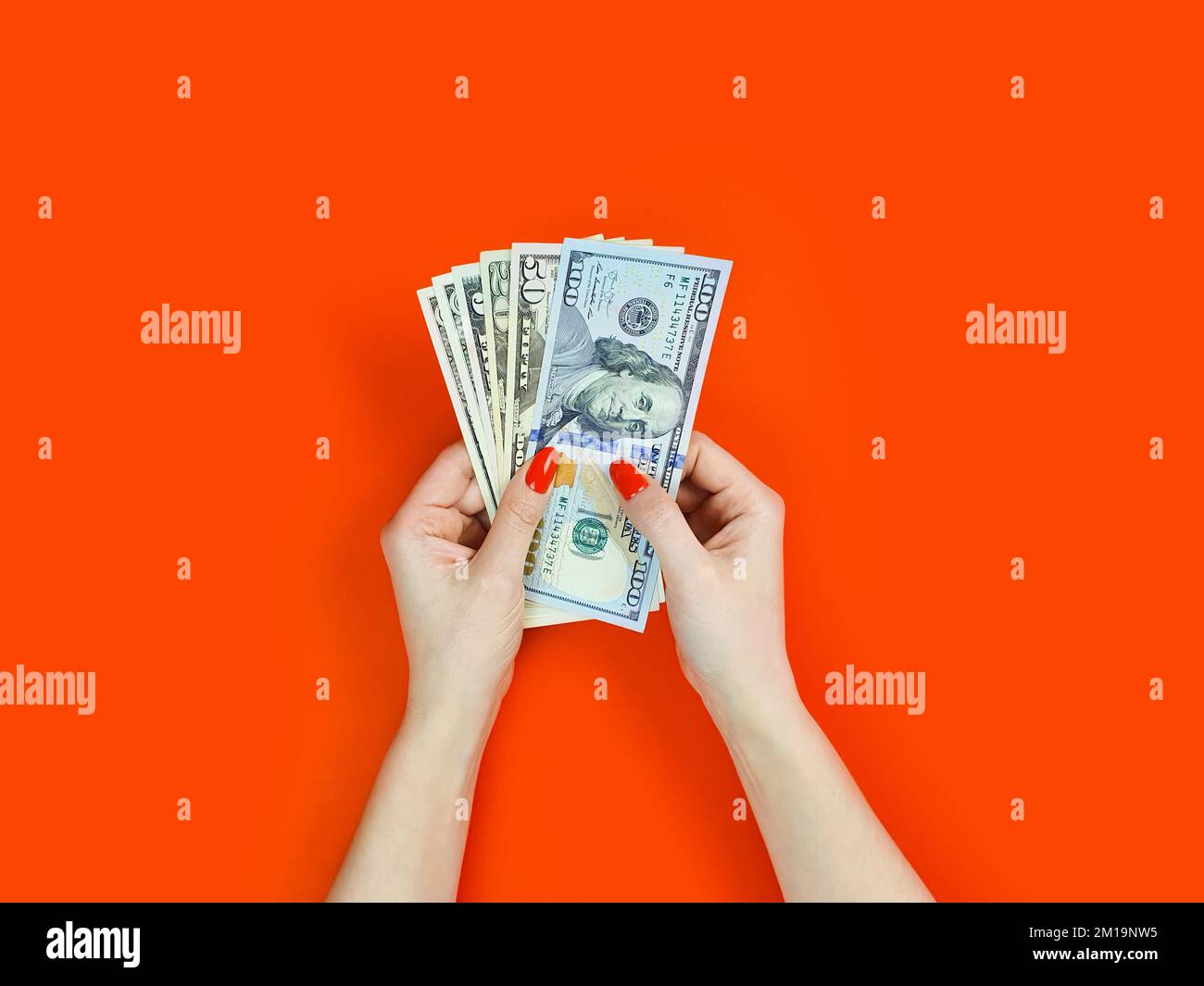 Dollarscheine in weiblichen Händen mit roter Maniküre auf rotem Hintergrund. Draufsicht auf Geld Stockfoto