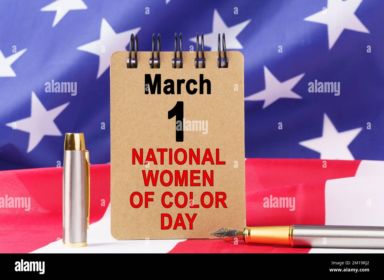 USA-Feiertage. Vor dem Hintergrund der US-Flagge liegt Pappe mit der Inschrift "NATIONAL WOMEN OF COLOUR DAY" Stockfoto
