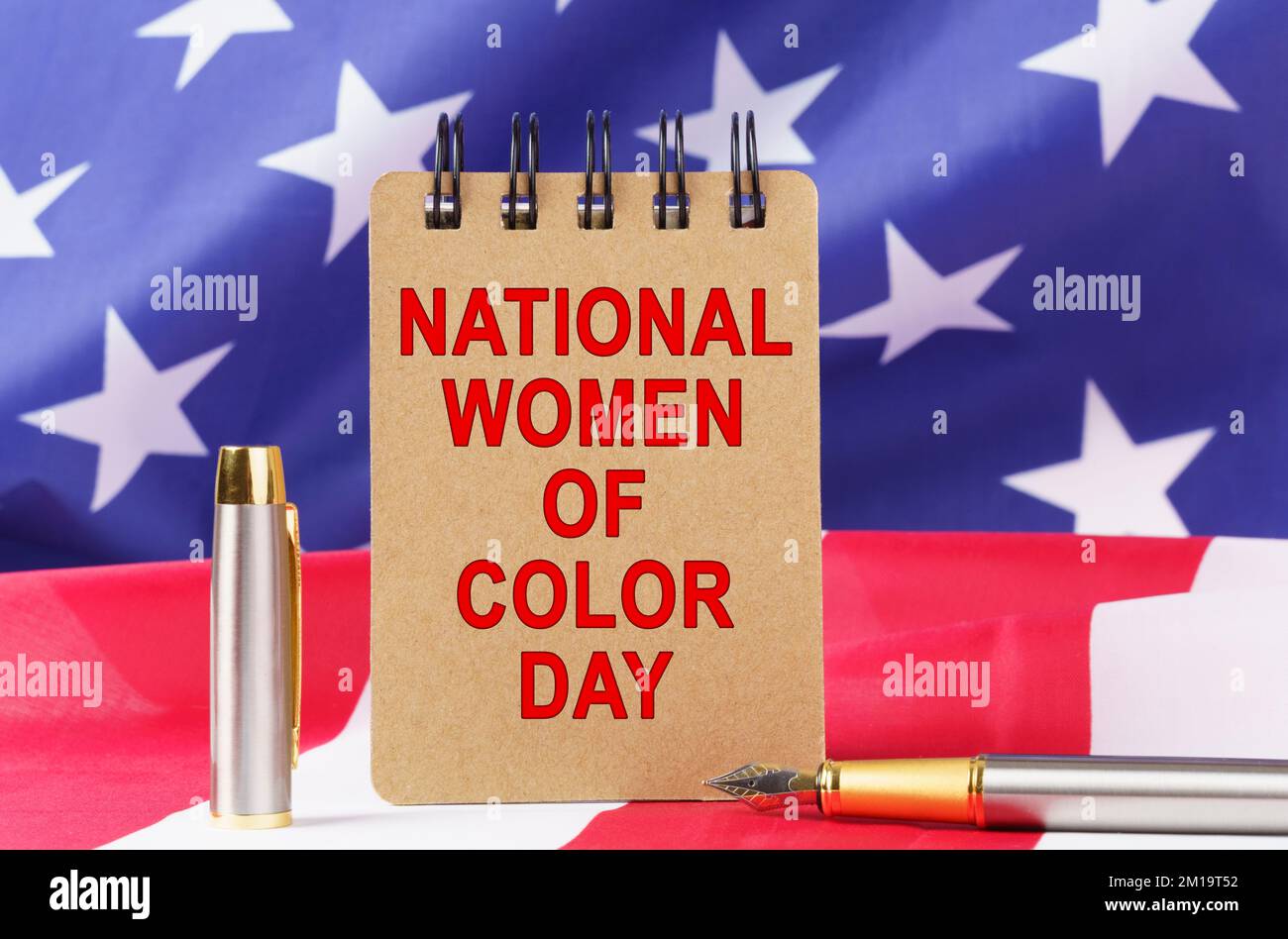 USA-Feiertage. Vor dem Hintergrund der US-Flagge liegt Pappe mit der Inschrift "NATIONAL WOMEN OF COLOUR DAY" Stockfoto