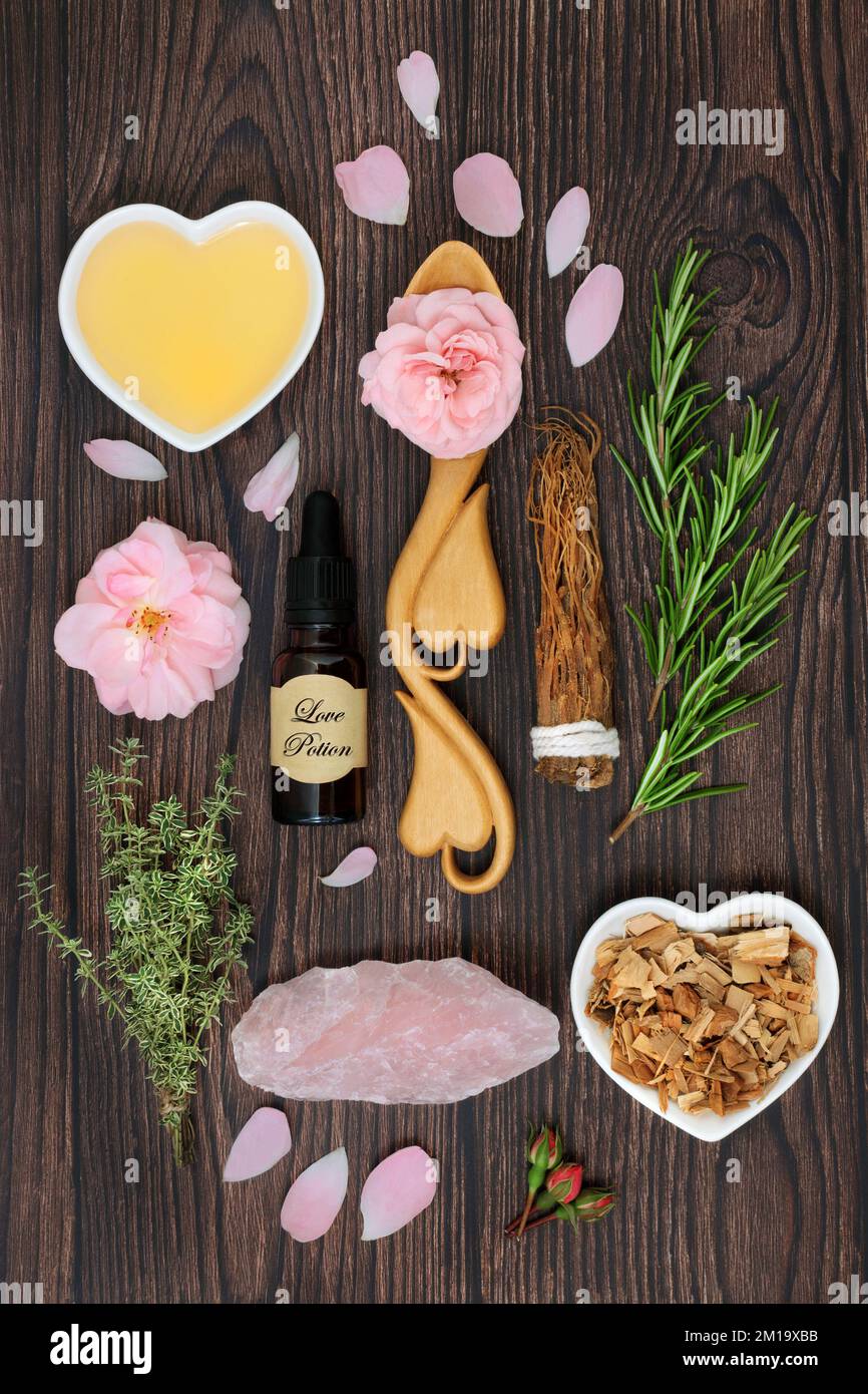 Liebestrank und aphrodisiakische Zutaten für magischen Zauber mit Kräutern, Rosenblüten, Honig, Gebräu in einer Flasche und Rosen-Quarz-Kristall. Stockfoto