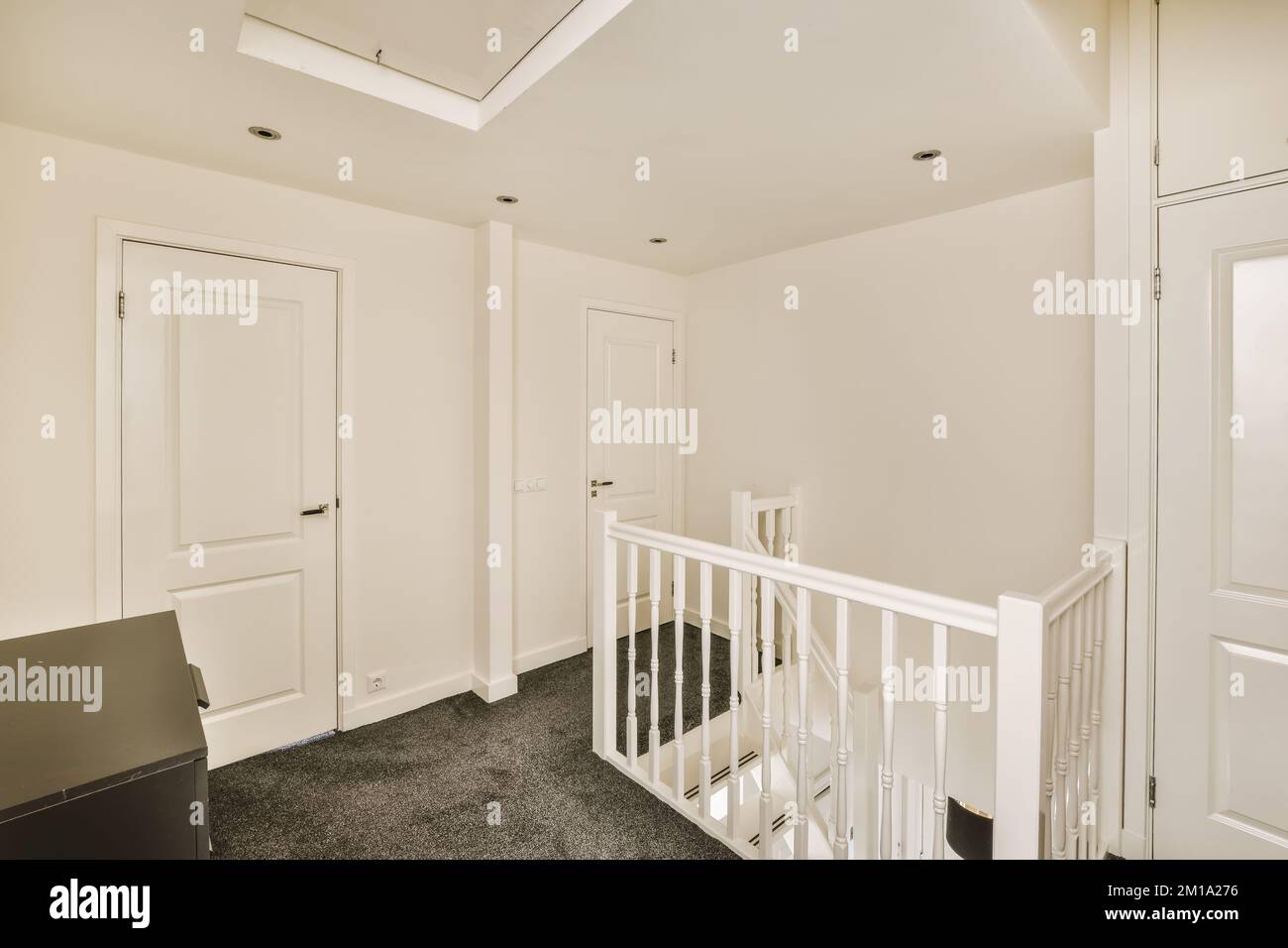 Ein leerer Raum mit weißen Wänden und schwarzem Teppichboden, es gibt eine Treppe, die in die zweite Etage führt Stockfoto