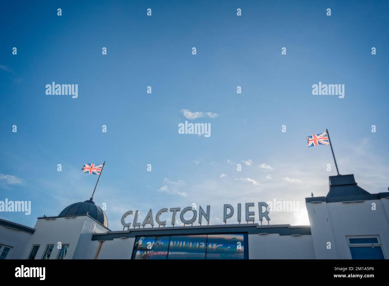 Eintritt zum Clacton/Clacton-on-Sea Pier, mit Gewerkschaftsflaggen über ihm, vor einem blauen Himmel mit weißer Wolke. Stockfoto