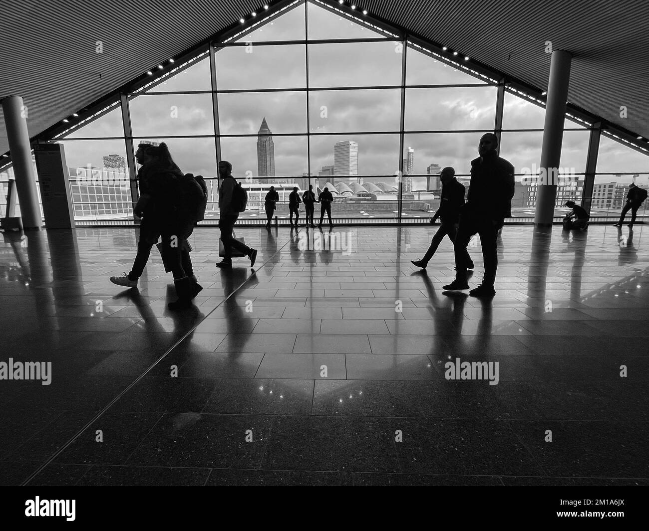 Menschen, die in einem modernen Gebäude mit der Frankfurter Stadt im Hintergrund spazieren gehen. Stockfoto