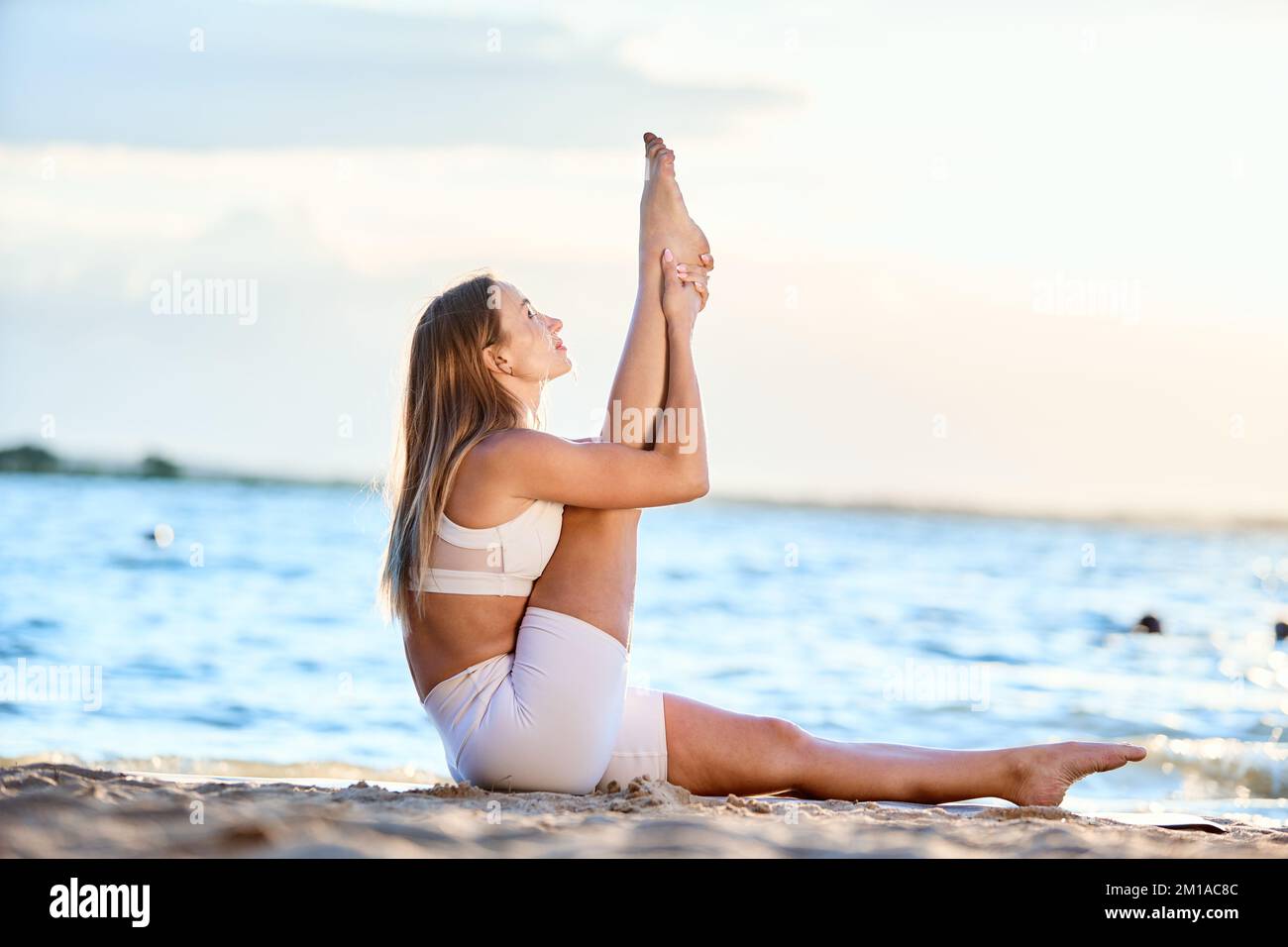 Junge Frau, die Yoga am Flussufer praktiziert. Stockfoto