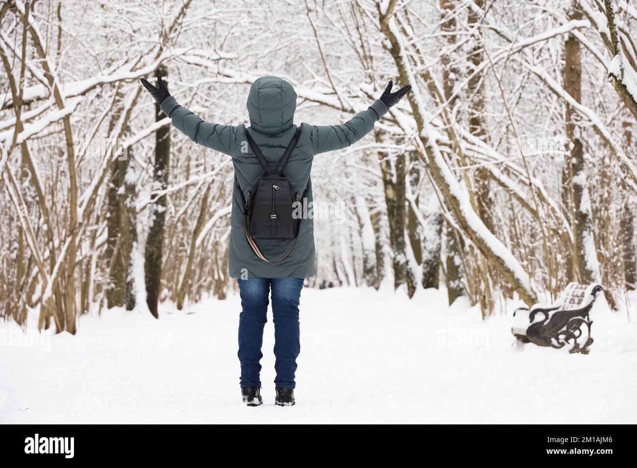Eine Frau mit Daunenjacke, die mit erhobenen Händen steht und das schneebedeckte Wetter genießt. Freizeit im Winterpark, kalte Jahreszeit Stockfoto