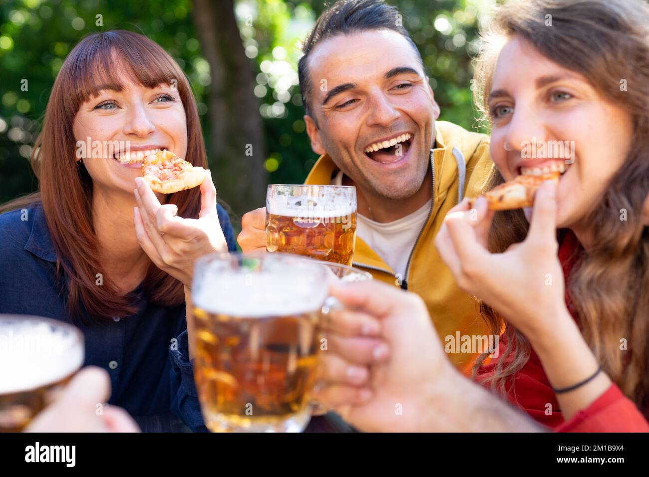 Fröhliche Freunde, die draußen auf Biergläser toasten - eine Gruppe von Freunden, die draußen im Pub Bier trinken Stockfoto